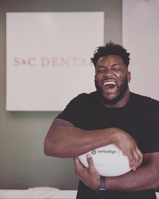 A man with a bright smile holds a white soccer ball at S&C Dental in Scottsdale, AZ