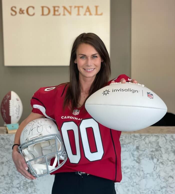A woman in a red jersey, Dr. Bri Stoterau, holds a rugby ball and helmet in Scottsdale, AZ