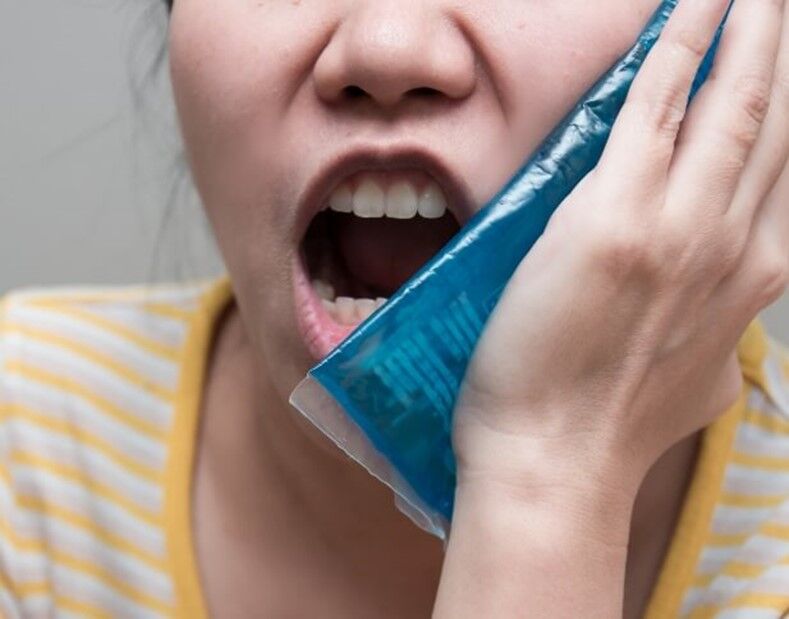 A person holding a blue ice pack on their mouth