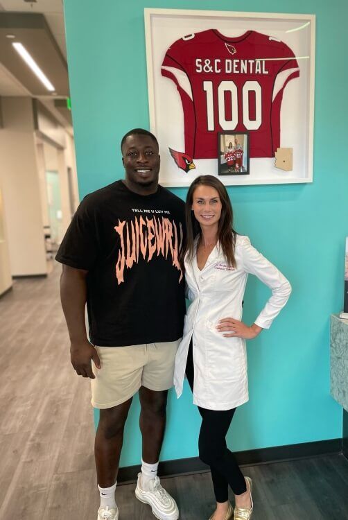 Dr. Bri with a patient in front of Arizona Cardinal Jersey at S&C Dental
