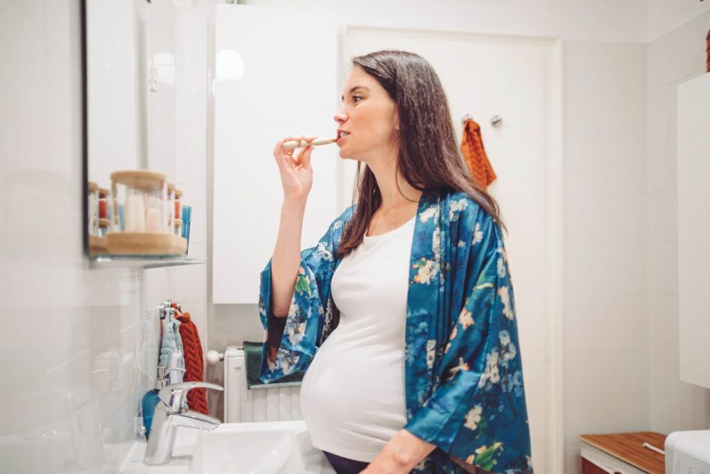 A pregnant person brushing her teeth in the bathroom